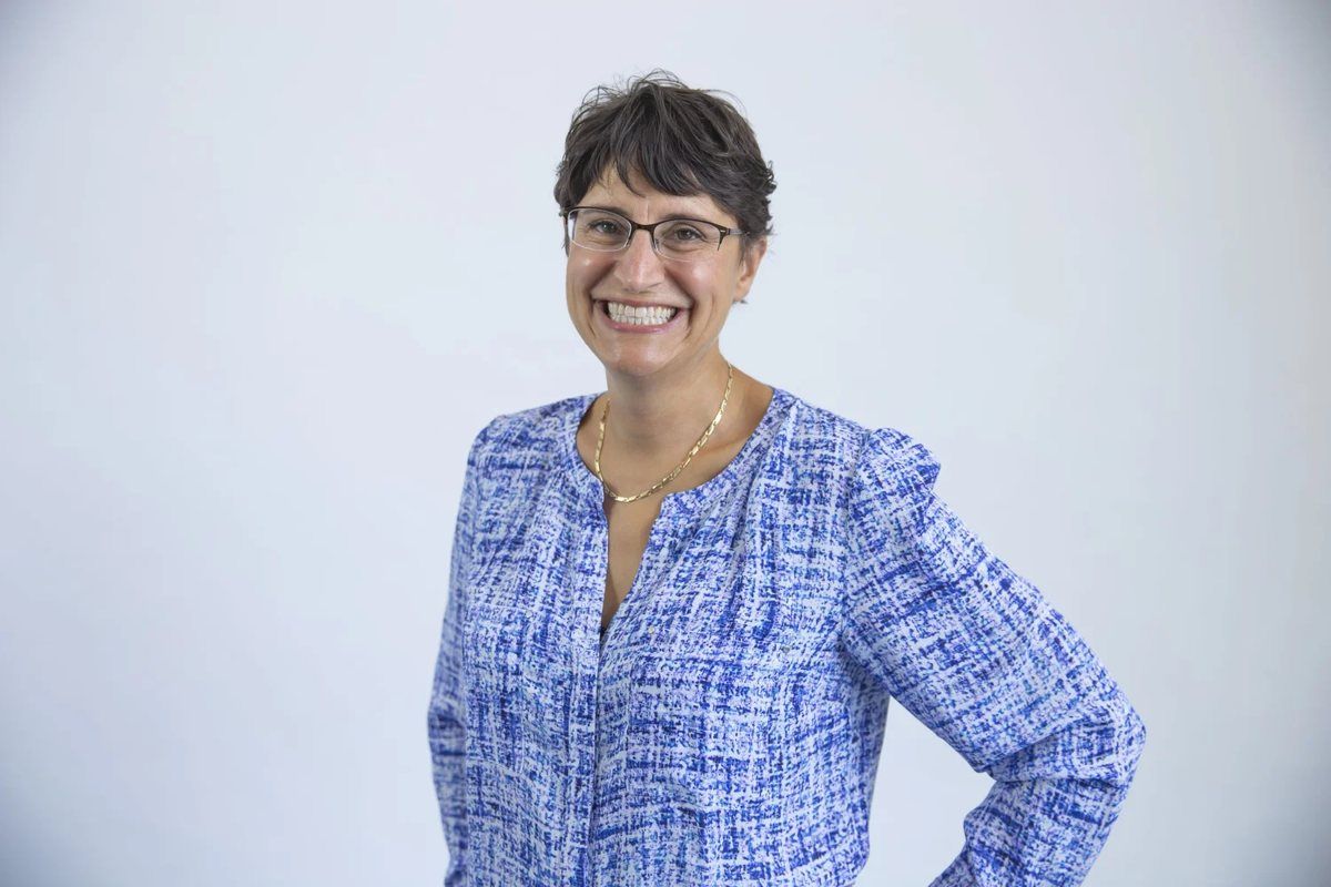 Team headshot of a woman in a patterned blouse on a light backdrop